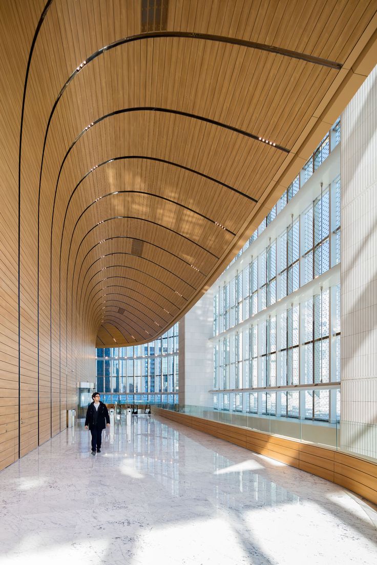 two people walking in an empty building with large windows on the walls and wood paneling