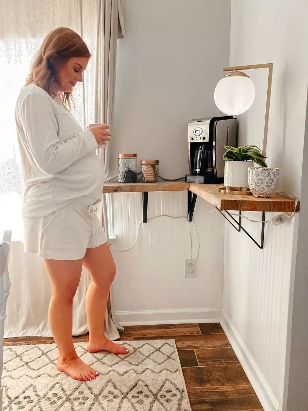 a woman standing in front of a coffee maker on top of a rug next to a window