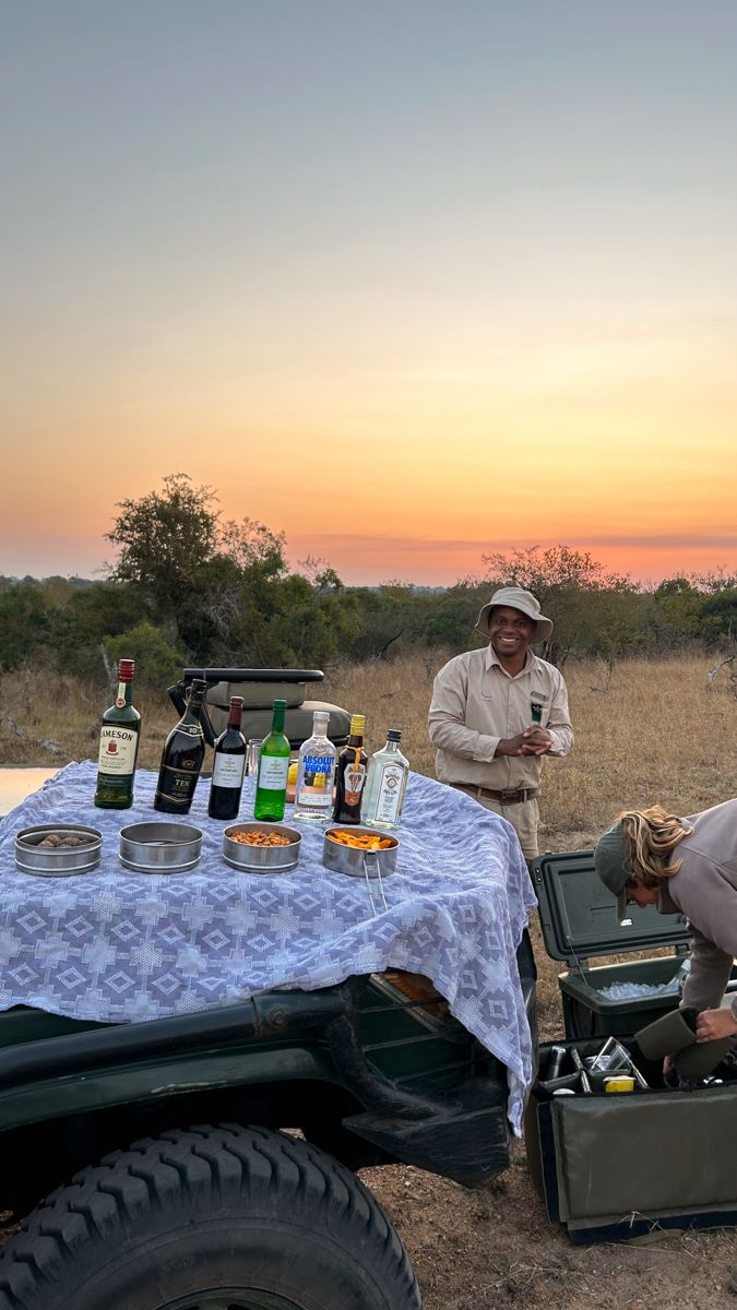 two men standing next to a table with drinks on it in the middle of a field