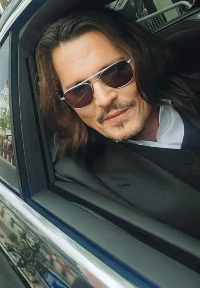 a man with long hair and sunglasses sitting in a car