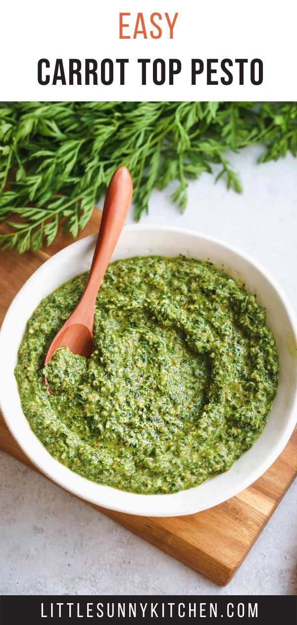 a white bowl filled with pesto on top of a wooden cutting board next to carrots