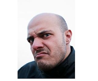 a bald man wearing a black jacket looking at the camera with an angry look on his face