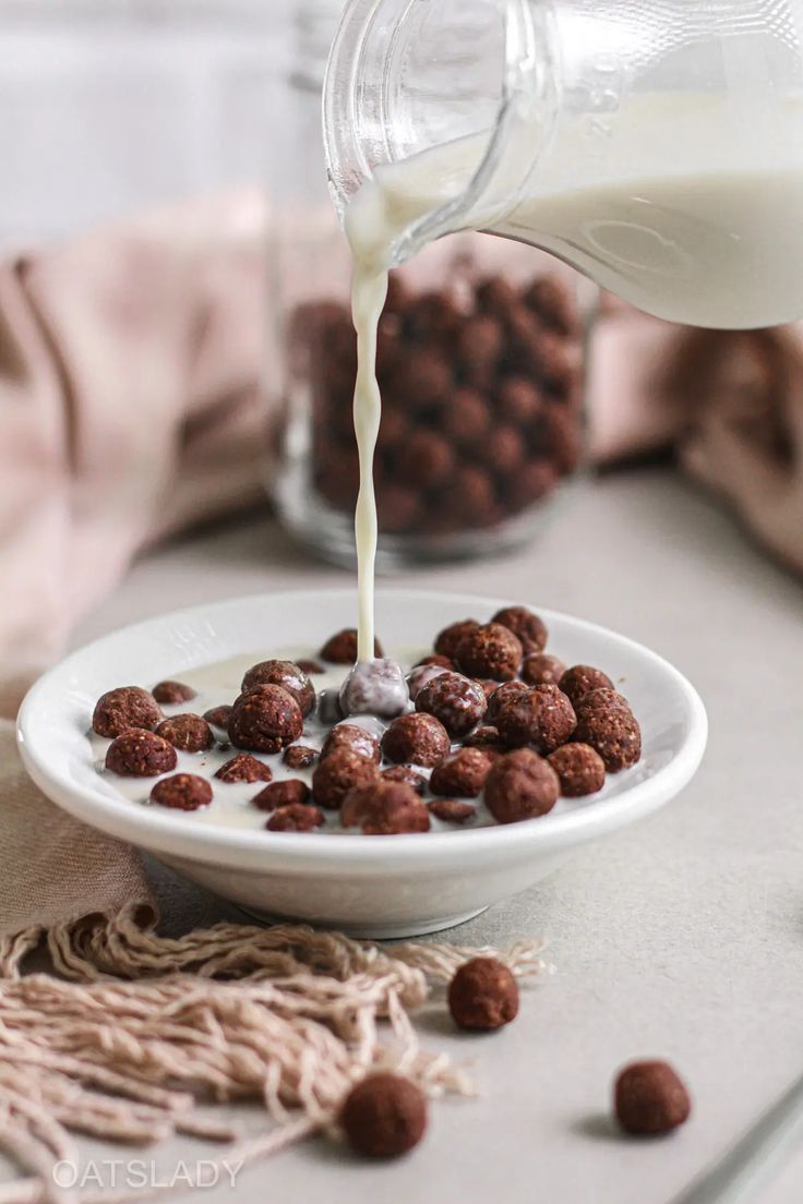 milk being poured into a bowl filled with chocolate covered cereals and oatmeal