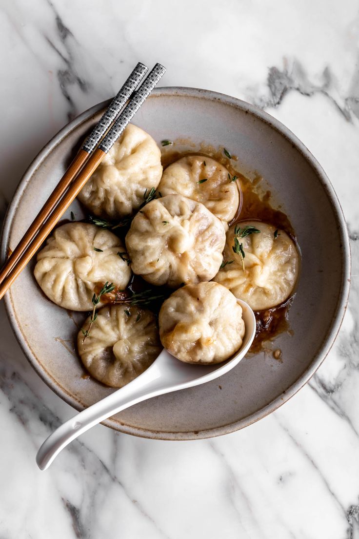 dumplings with sauce and chopsticks in a white bowl on a marble table