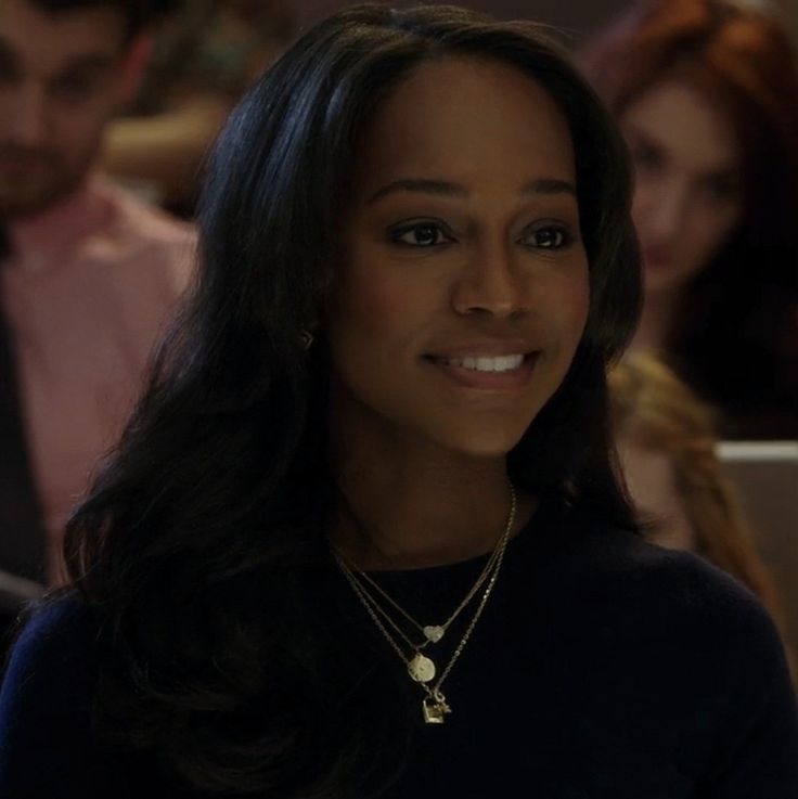 a woman with long hair wearing a black shirt and gold necklace smiling at the camera