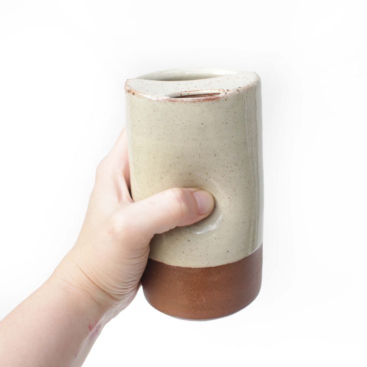 a hand holding a ceramic cup with brown rims on it's side, against a white background