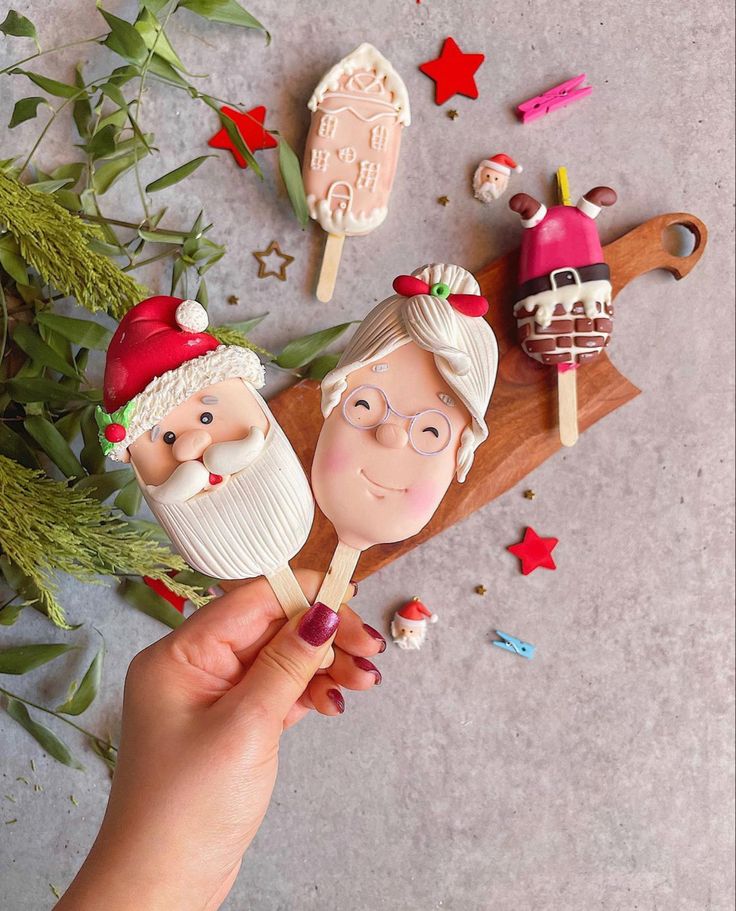 a person is holding some christmas decorations on top of a wooden board with santa and mrs claus