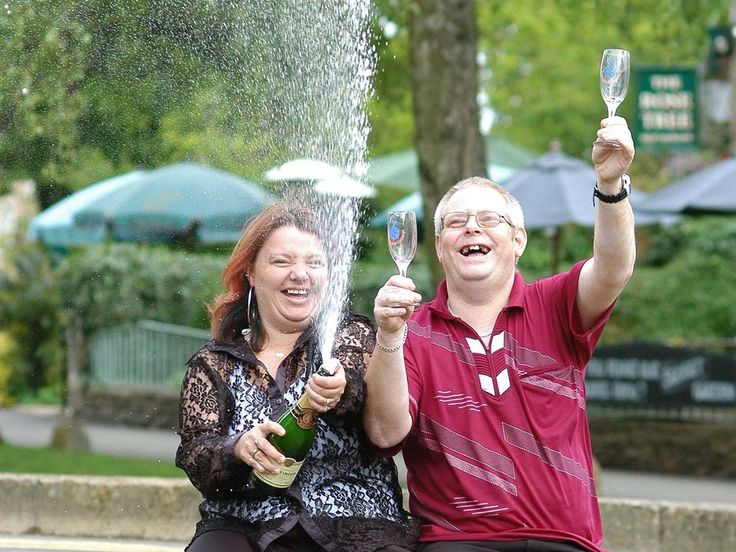 a man and woman holding up wine glasses in front of a sprinkler