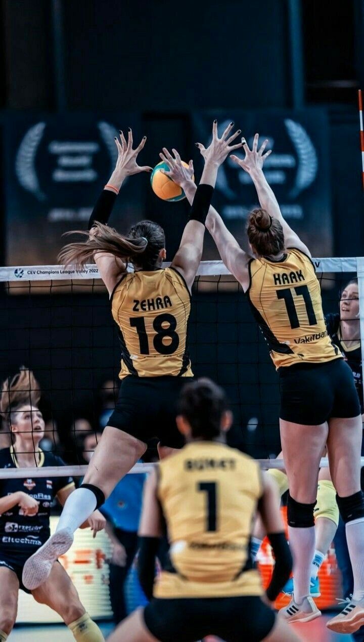 two women playing volleyball in front of the net with their hands up to block the ball