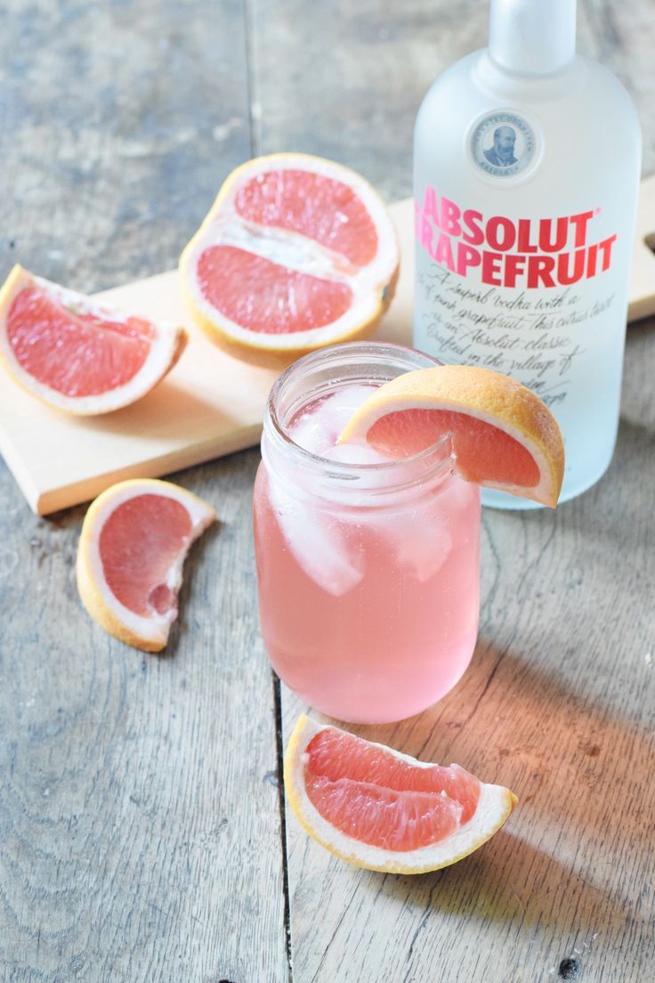 grapefruit and gin on a wooden table next to a bottle