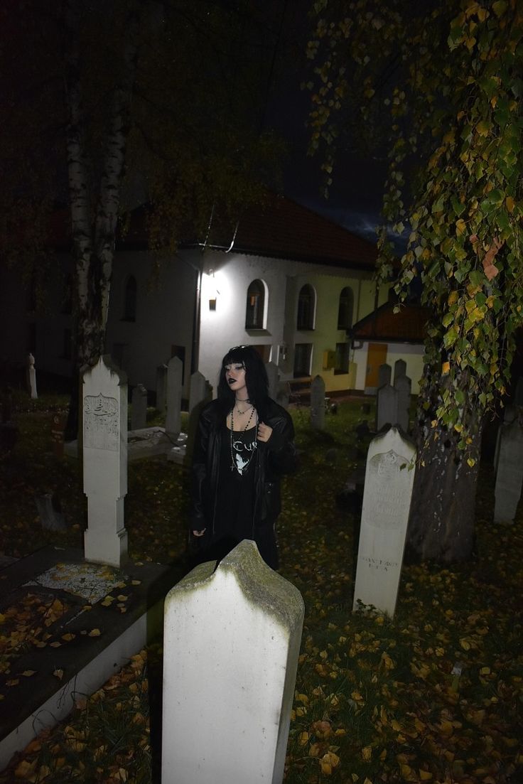 a woman standing in the middle of a cemetery at night with her hands on her chest