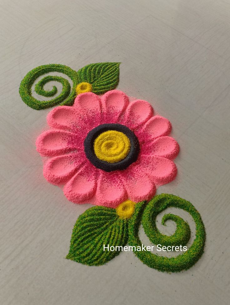 a pink flower with green leaves and swirls on the bottom is made out of felt