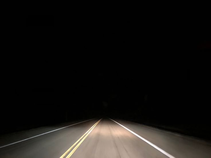 a car driving in the dark on a highway at night with its headlights turned down