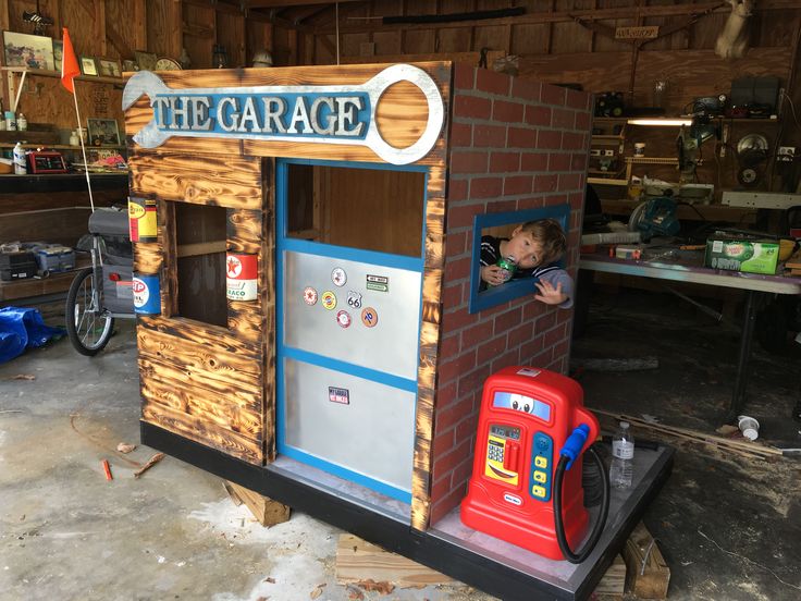 a child in a toy house made out of bricks and wood with the word garage written on it