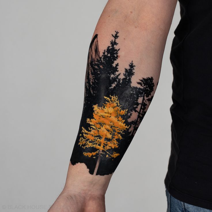 a man's arm with an orange tree on it and yellow leaves in the background