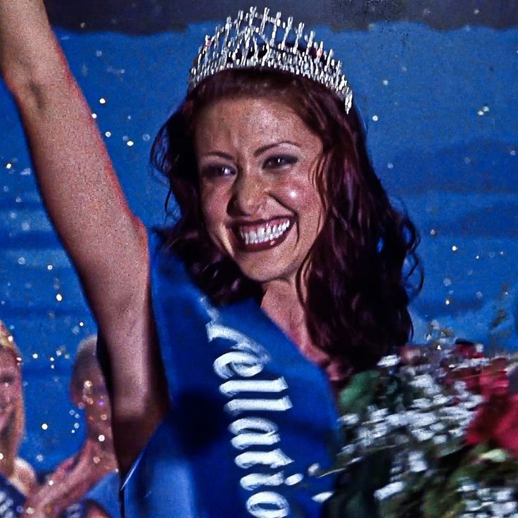 a woman wearing a tiara and smiling at the camera with her arms in the air