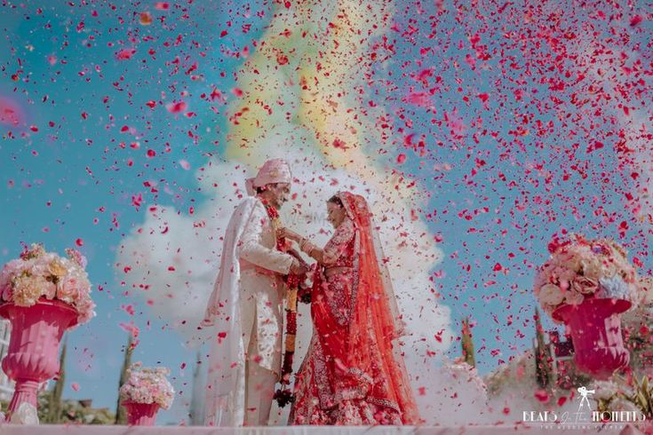 a newly married couple standing in front of flowers and confetti thrown from the sky