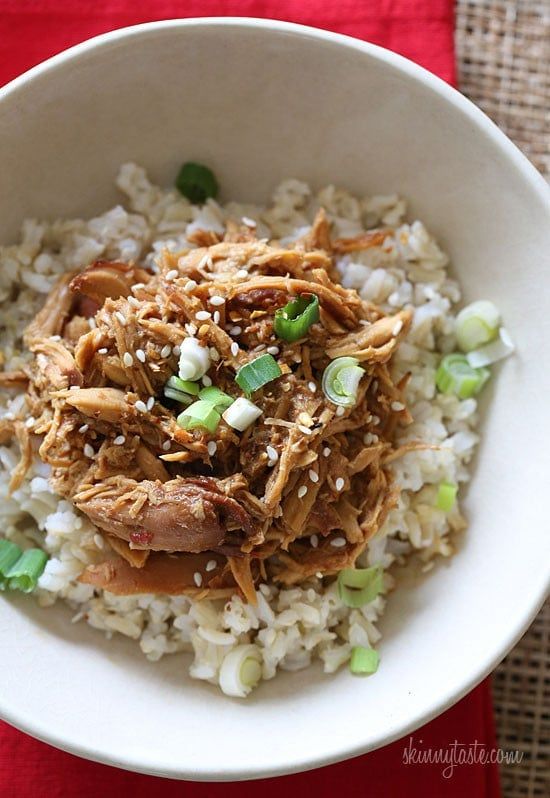 a white bowl filled with rice and meat on top of a red table cloth next to a fork