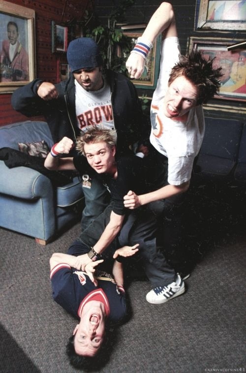 three young men standing and laying on the floor in front of a couch with their arms around each other