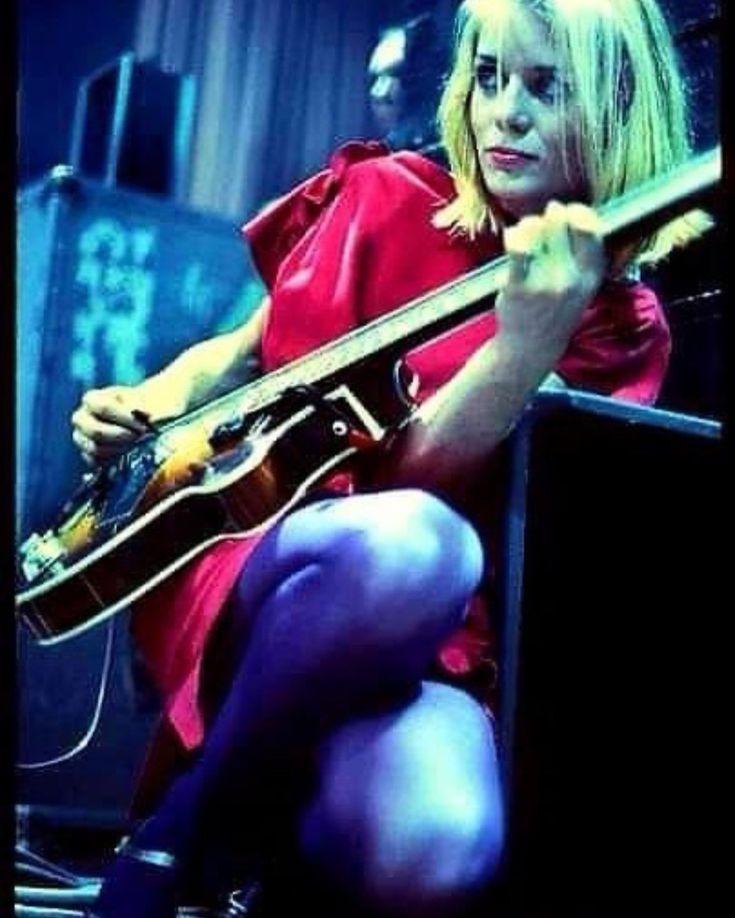 a woman sitting on the ground with a guitar in her hand and wearing tights