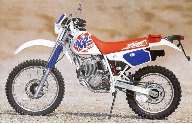 a red, white and blue dirt bike parked on gravel