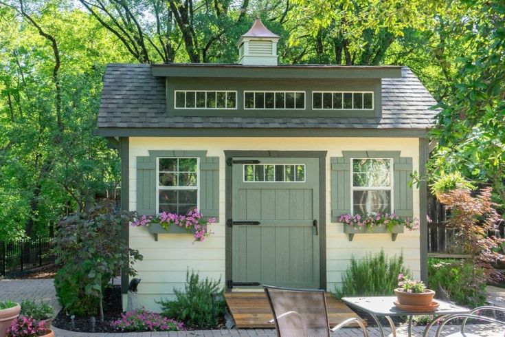 a small shed with flowers and potted plants on the outside, along with patio furniture