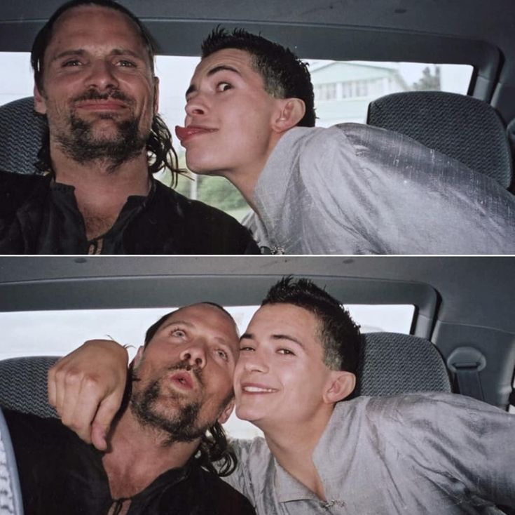 two men sitting in the back seat of a car, one is kissing the other