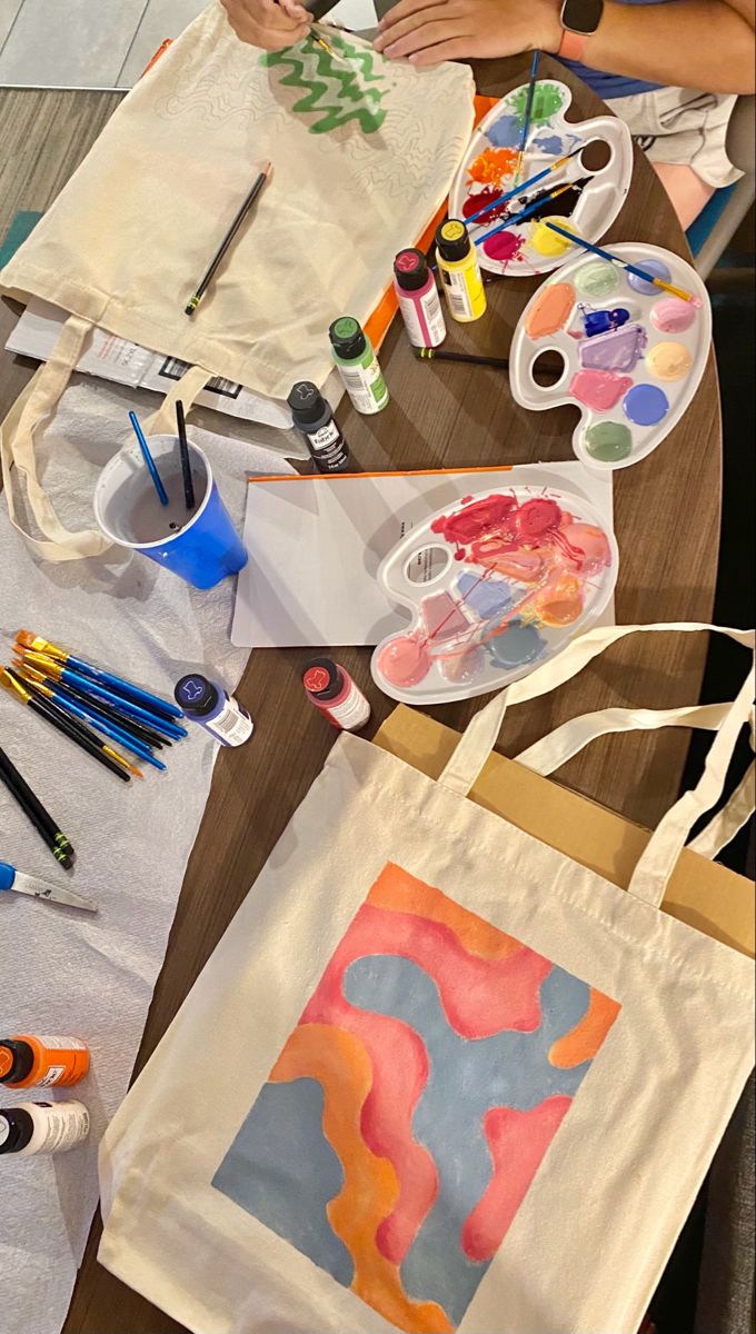 a person is painting on a canvas bag with watercolors and paintbrushes