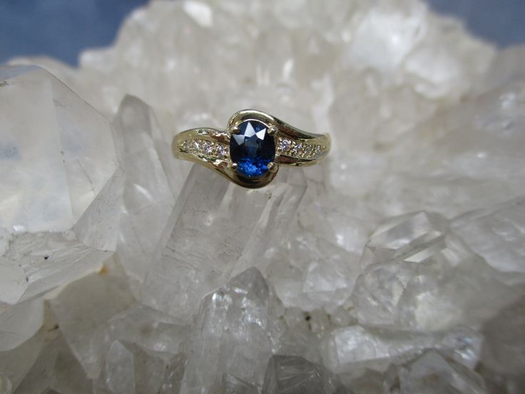 This 14K Gold Ring is set with a beautiful gem grade Sapphire and accented with Diamonds. The Oval Cut Sapphire has great blue color. Not too dark and not too light. It measures 5.5 mm by 4.5 mm and weighs .66 carat. It is a clean, well cut natural stone. There are 8 accenting Diamonds, 4 on each side. The accent Diamonds weigh .05 carat total weight. The ring is about 5/16 inch wide on top and tapers to a narrow band in the back. Low profile settings make this a very wearable ring. It is made i Sapphire Ring With Diamond Gemstone Accents, Blue Oval Birthstone Ring With Diamond Accents, Dazzling Sapphire Gemstones For Anniversary, Formal Sapphire Diamond Ring With Gemstone Accents, Heirloom Sapphire Ring With Diamond Gemstone Accents, Diamond Sapphire Ring With Gemstone Accents For Promise, Blue Diamond Ring With Gemstone Accents, Oval Shape, Diamond Sapphire Ring For Promise, Blue Diamond Gemstones For Anniversary