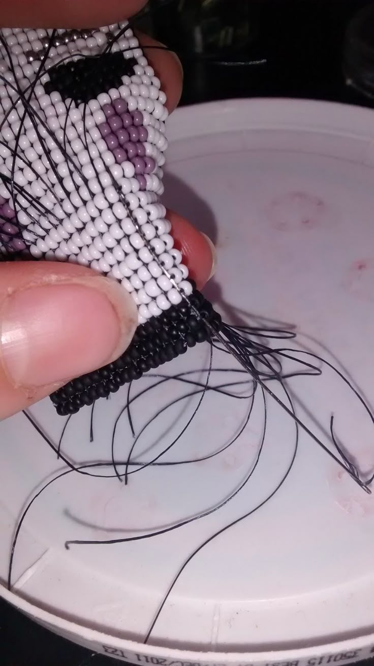 a person is stitching something on top of a white plate with black thread in it