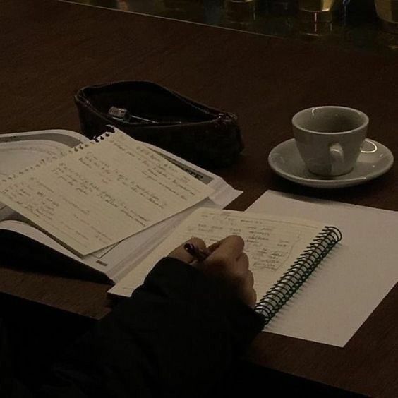 a person sitting at a table writing on paper next to a cup and saucer