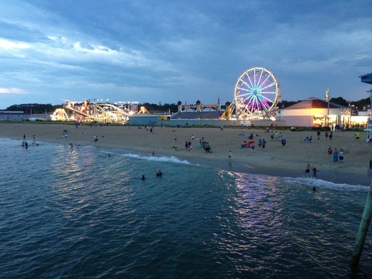 people are on the beach and in the water at night with ferris wheel in background