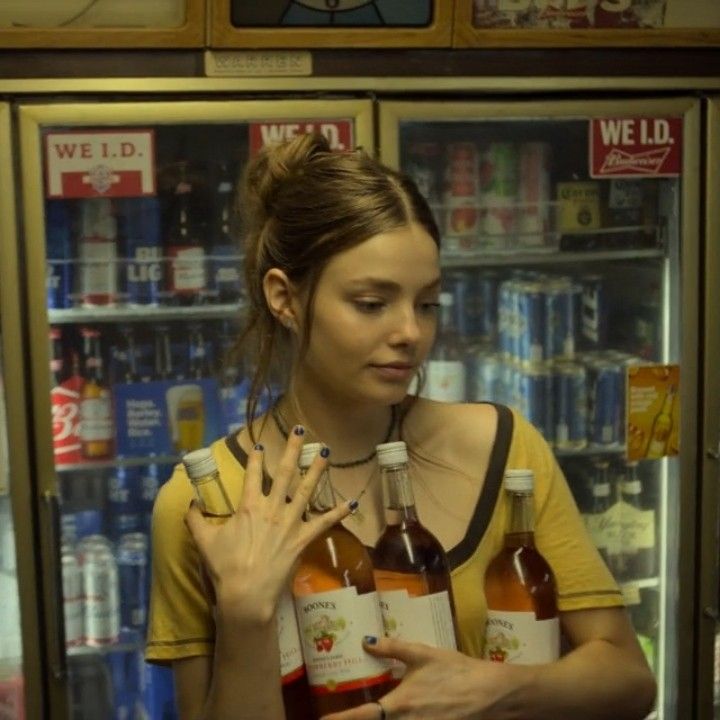 a woman standing in front of a vending machine holding two bottles of beer and looking at her phone