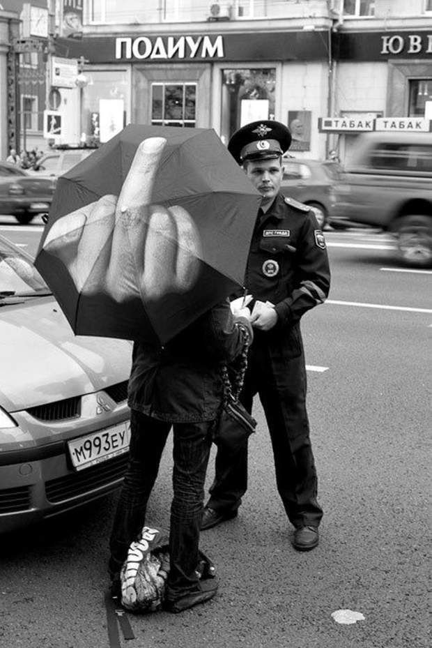 two people standing on the side of a road with an umbrella in front of them