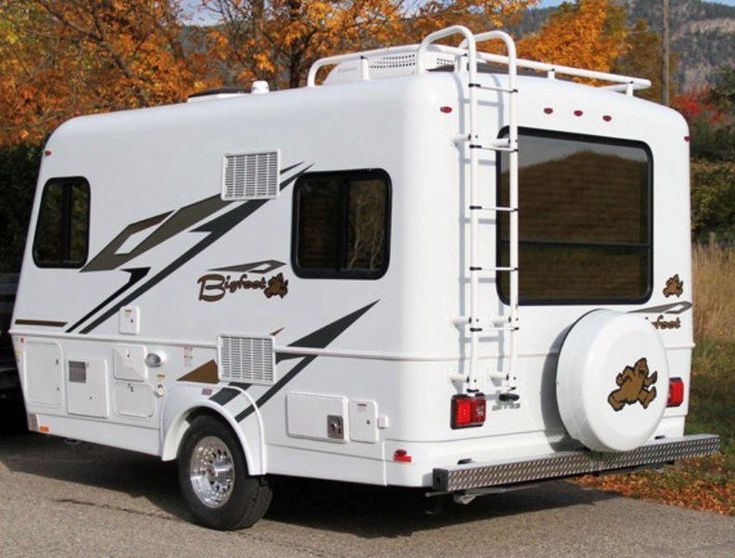 an rv is parked on the side of the road in front of some autumn trees