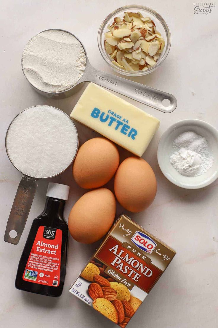 ingredients to make almond cake laid out on a white counter top, including eggs, flour, butter and other items