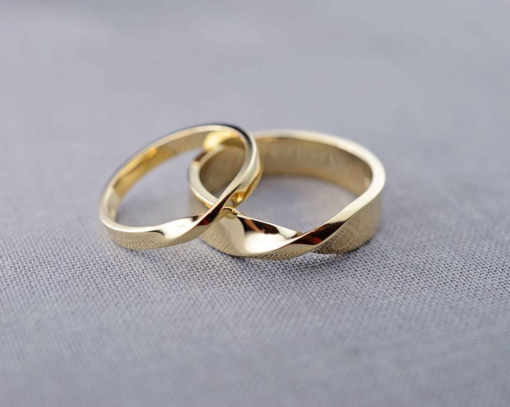 two wedding rings sitting on top of each other in front of a gray background,