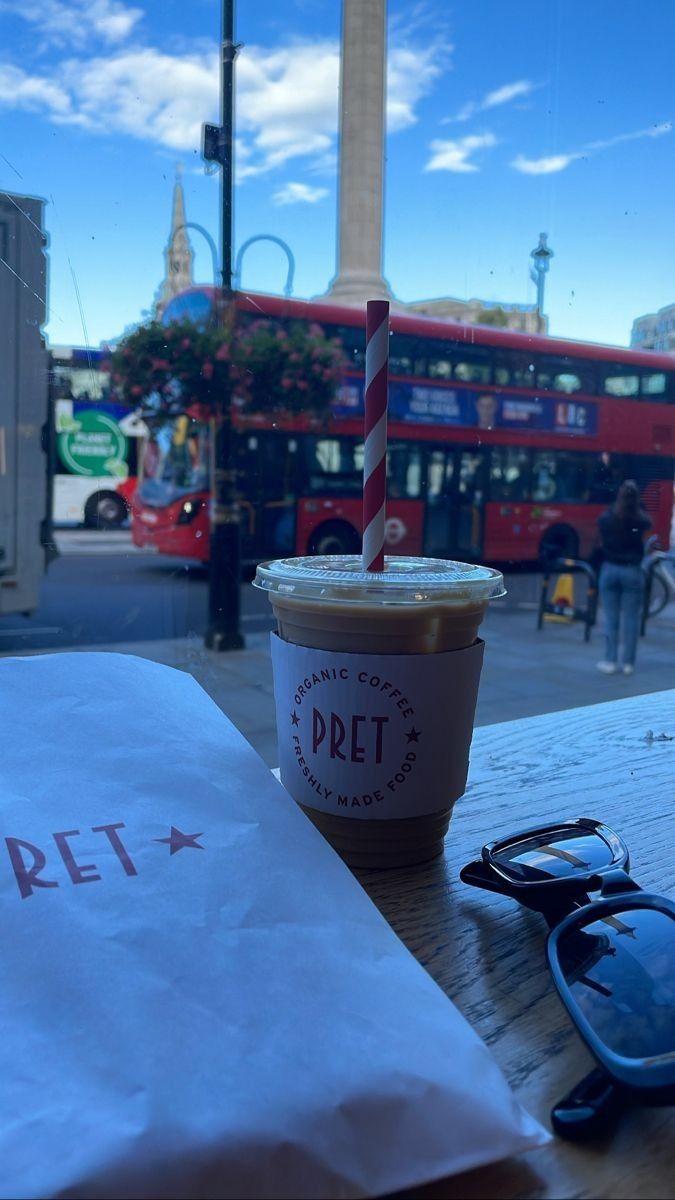 a cup of coffee sitting on top of a wooden table next to a paper bag