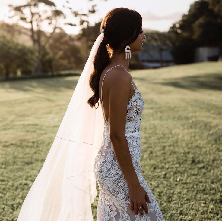 a woman in a wedding dress standing on the grass with her veil over her head