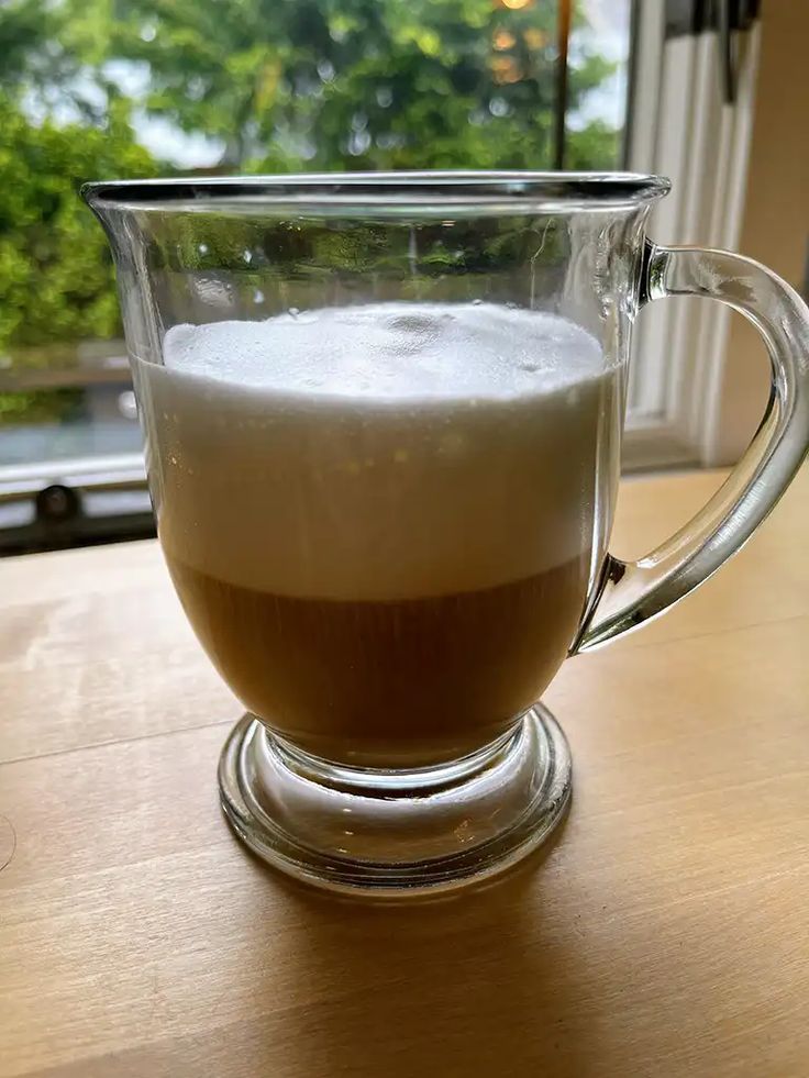 a glass cup filled with liquid sitting on top of a wooden table next to a window