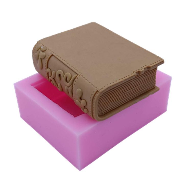 a pink and brown book shaped object sitting on top of a purple block with writing