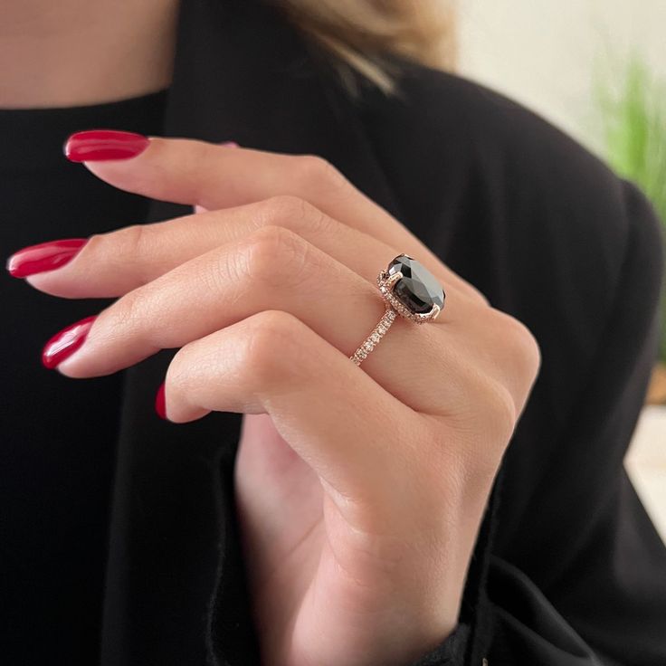 a woman's hand wearing a ring with a black diamond on it and red nails