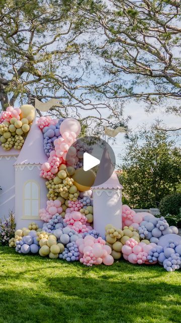 a house made out of balloons and flowers on the grass with trees in the background