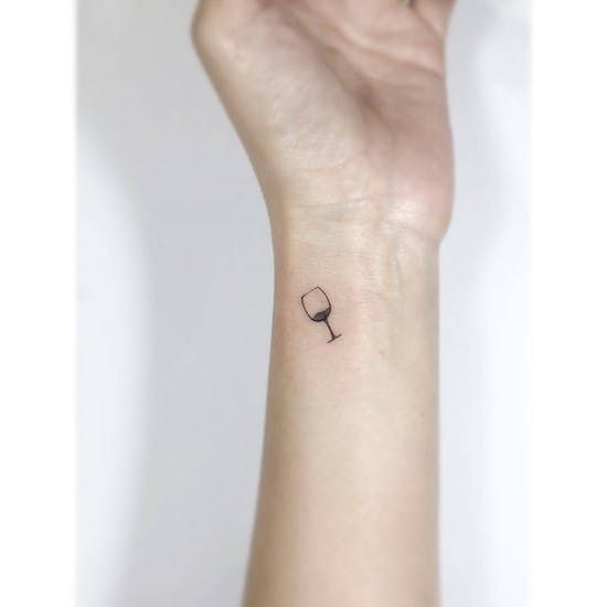 a woman's wrist with a small wine glass tattoo on the left side of her arm