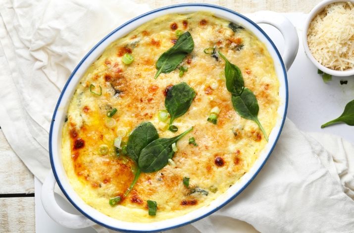 a casserole dish with spinach and cheese in it on a white table