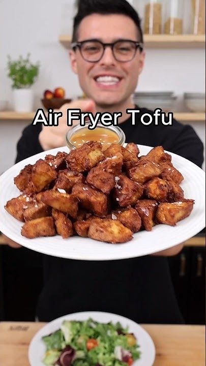 a man holding a white plate with fried food on it and the caption air fryer tofu