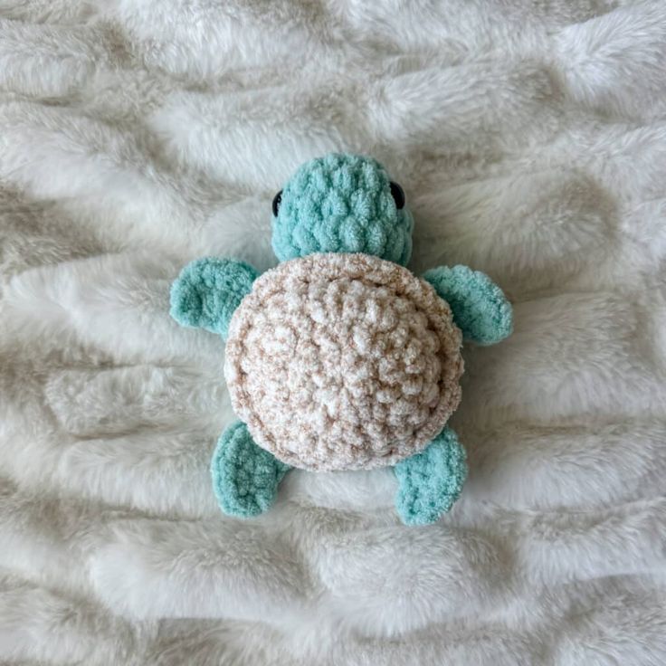 a crocheted turtle laying on top of a white blanket