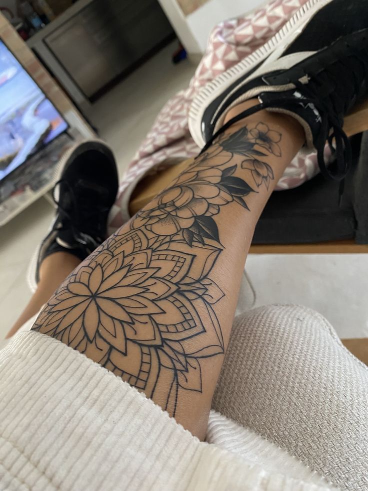 a person with a tattoo on their leg sitting in front of a computer desk and television