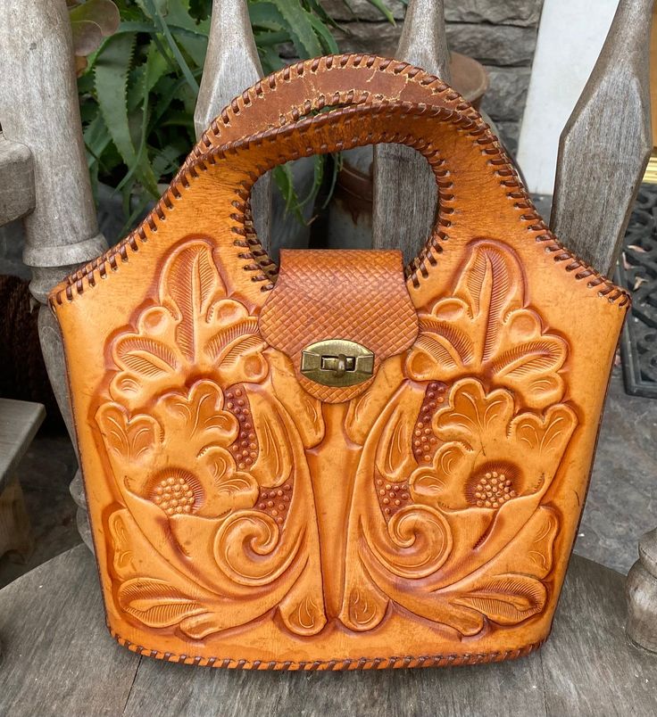 This vintage leather hand tooled bucket bag/horse bag is a true gem from the 1970s. With its beautiful brown color and western look, it is the perfect accessory for any vintage lover. The bag measures 12" x 11" and is made of high-quality leather. There are some minor stains at the bottom edge as [picture shows....the inside leather lining of the handles has major wear and tear as picture shows... The bag's unique design and originality make it a great addition to any collection. Its origins can be traced back to the United States, where it was crafted with great care. It is perfect for carrying your essentials and making a statement. There are normal signs of wear for an item over 50 years, like creases on the handle and finish wear to the brass twist snap. The inside zipper pocket still Vintage Tooled Leather Purse, Tooled Leather Handbags, Vintage Hand Tools, Tooled Leather Bag, Tooled Leather Purse, Colorful Handbags, Boho Hippie Chic, Beautiful Handbags, Hand Tooled Leather