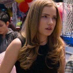 a girl with long brown hair standing in front of balloons and other people behind her